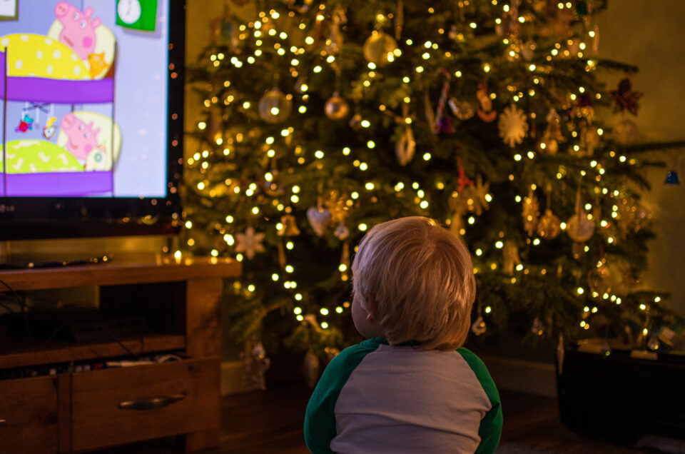 A little boy watching Peppa Pig with a Christmas Tree in the background.