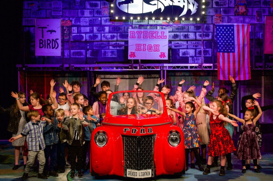 A group of children performing on stage to the musical Greece.