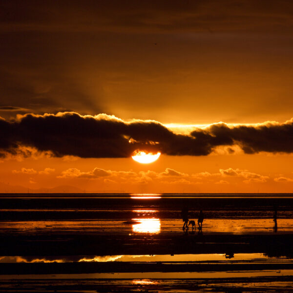 A family on the beach at St Anne's with the sun setting in the background.