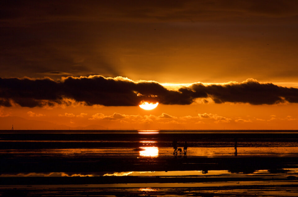 A family on the beach at St Anne's with the sun setting in the background.