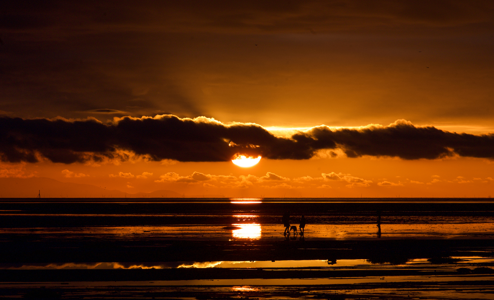 A family on the beach at St Anne's with the sun setting in the background.