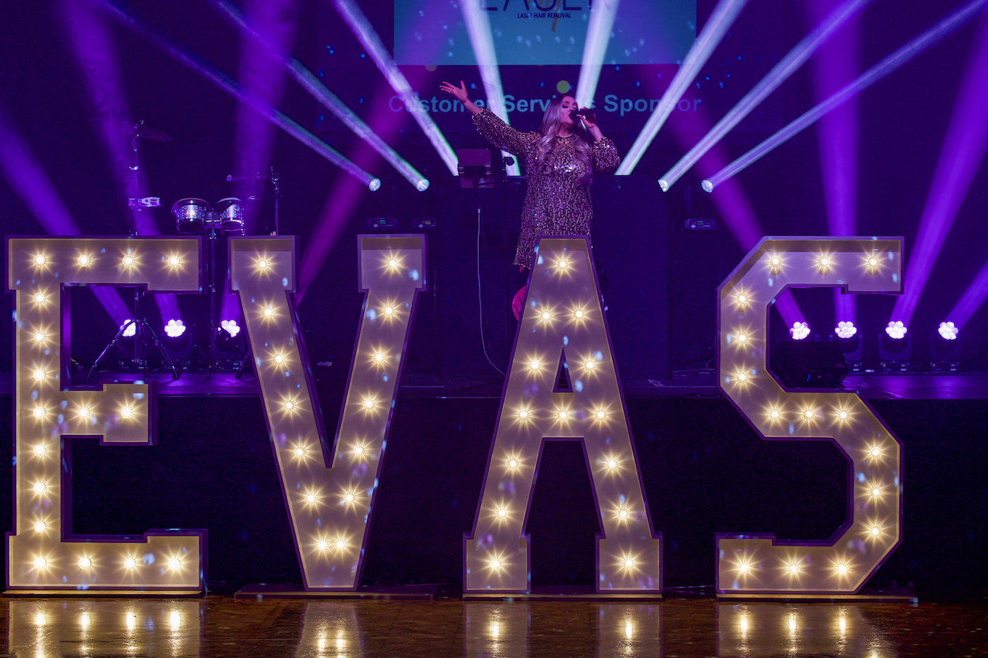 A lady singing in front of a lit EVAS sign.